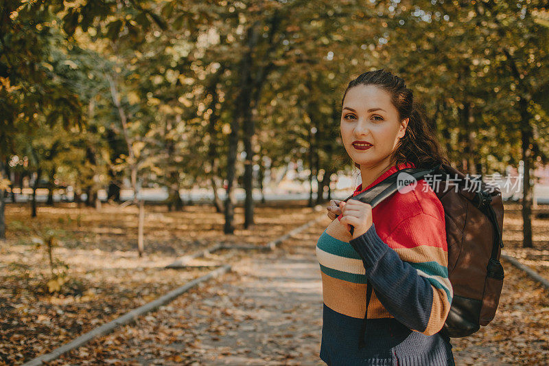 年轻的加码旅行家女孩与背包旅行沿着欧洲秋天城市，秋天公园。独自旅行，自由和积极的生活理念