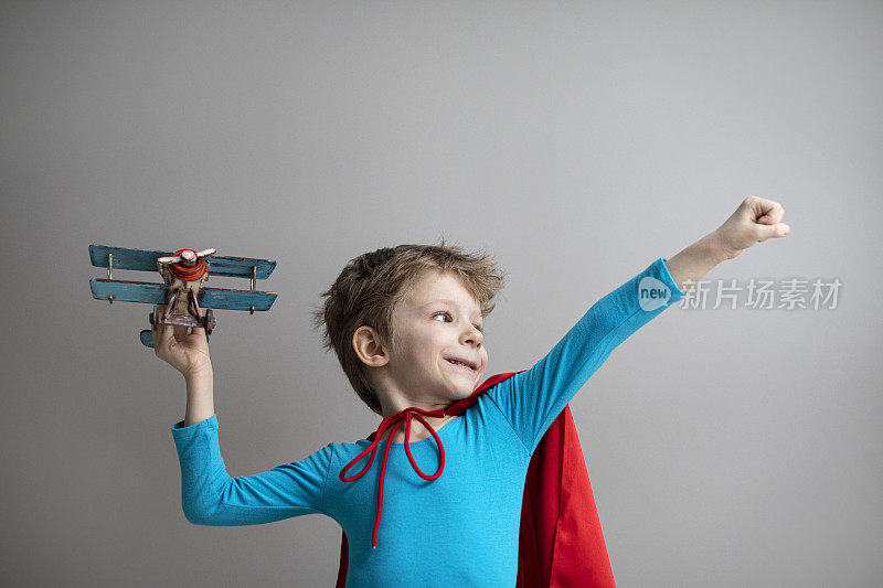 穿着红色斗篷的超级英雄小男孩在玩飞机。快乐微笑的孩子。成功、动力和旅行。