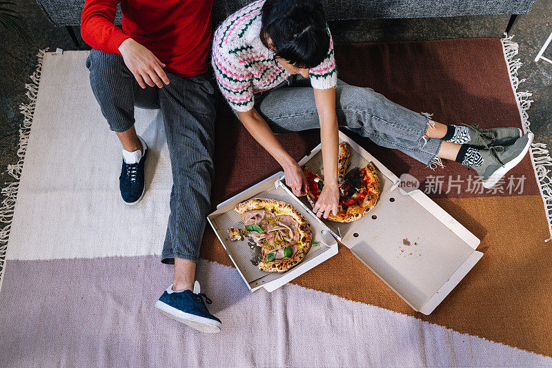 上图拍摄的是一对匿名夫妇坐在客厅的地板上，吃着他们最喜欢的面包店里的披萨