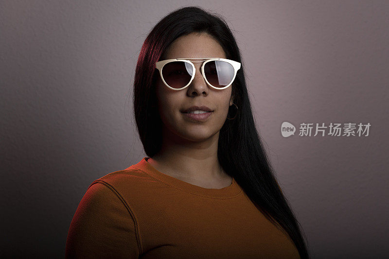 年轻的拉丁女人工作室肖像。她很严肃，戴着墨镜望着镜头。