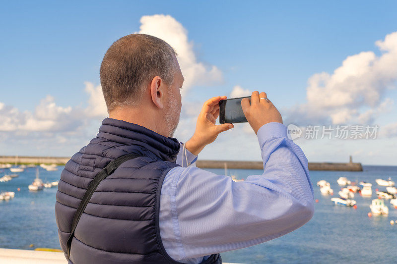 成熟的男游客用手机拍着大海的风景