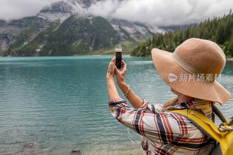 年轻女子在美丽的高山湖泊周围徒步旅行时拍照