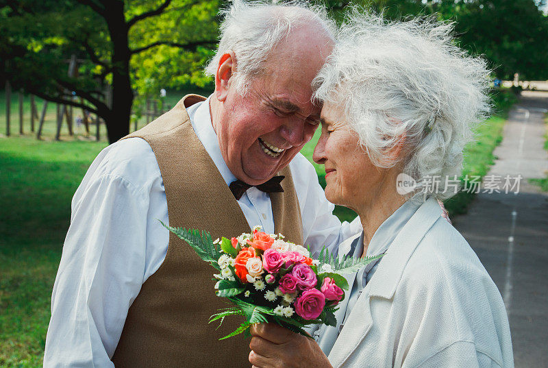 一对老夫妇在绿色的公园里散步。祖母和祖父在金婚纪念日庆典上。爷爷奶奶笑了。50年的浪漫爱情故事。黑色和白色。