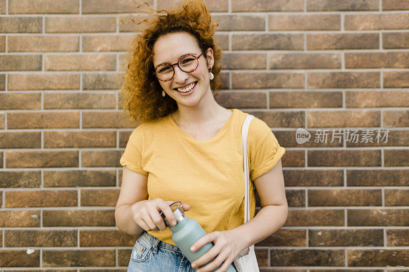 红发妇女用可重复使用的水瓶喝水，用可重复使用的棉生态生产袋购物。零废物生活方式概念