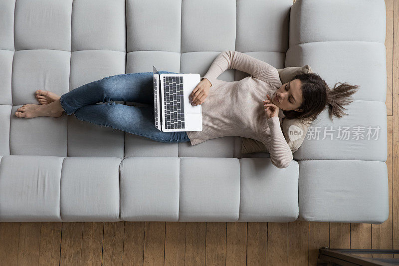 沉思严肃的20岁女孩休息在沙发上，使用笔记本电脑