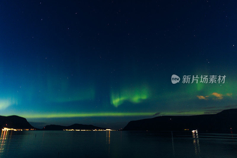 风景秀丽的北极光在峡湾和发光的城镇在挪威