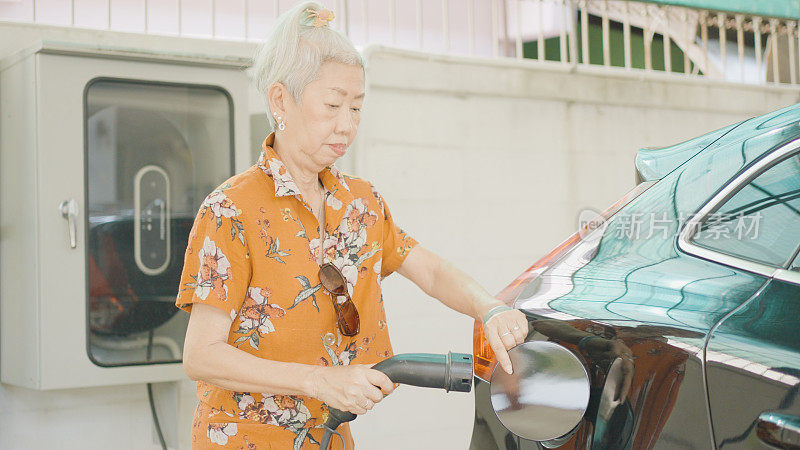 亚洲老年妇女在家里为她的电动车充电，可持续的生活方式