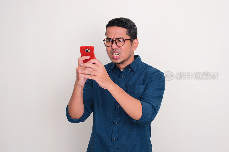 亚洲成年男子用手机发短信，表情愤怒