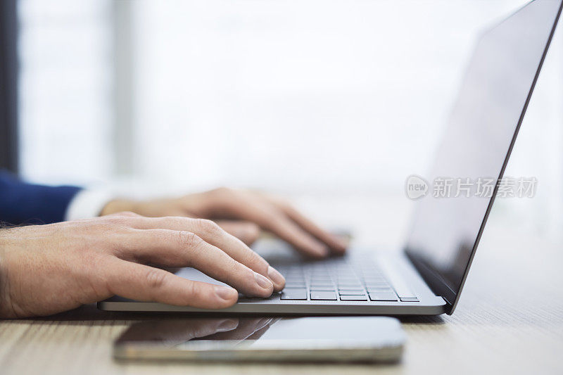 照片中，一名男子的双手近距离摆弄着一台现代笔记本电脑的键盘，背景是模糊的办公场景