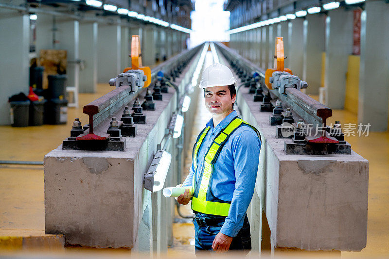 在工厂工作场所，专业工程师站在电气或空轨列车的铁轨之间的肖像。