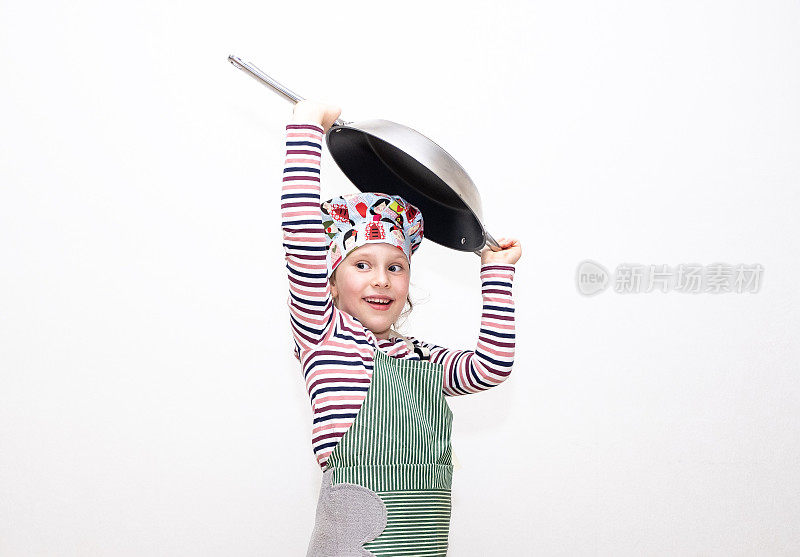 一个8岁的白人女孩打扮成厨师，双手拿着一只大煎锅举过头顶，很开心。