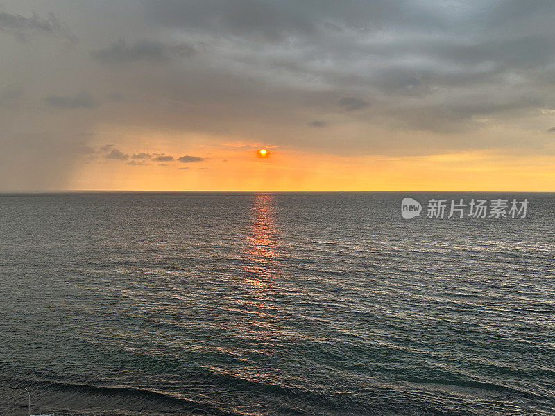 太阳在海洋地平线上戏剧性的橙色天空中落下的图像，忧郁的灰色云岸，太阳在水中的反射