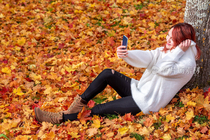 一名女子坐在地上自拍，欣赏秋景