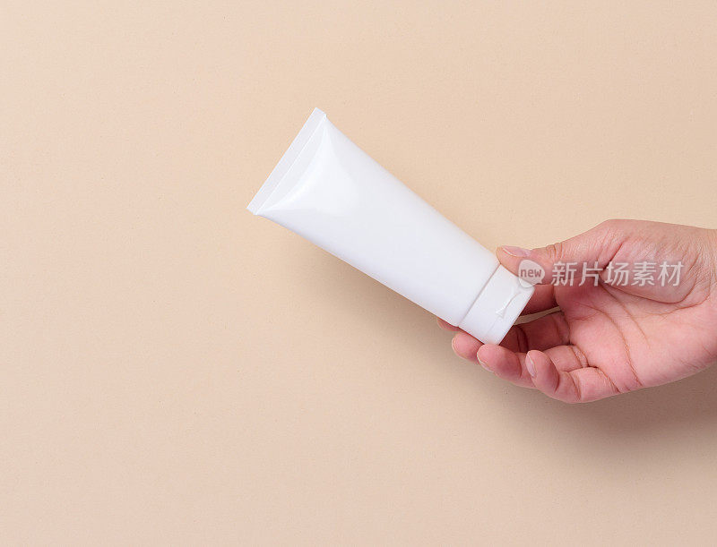 一个女人手里拿着一个白色的塑料管，里面装着米色背景的奶油和牙膏