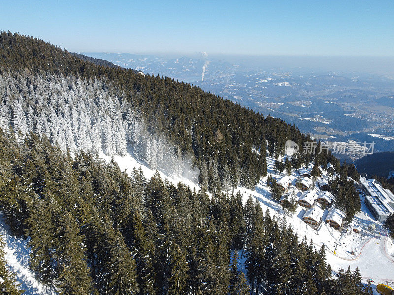 鸟瞰高山滑雪胜地，四周环绕着松树，天空湛蓝。