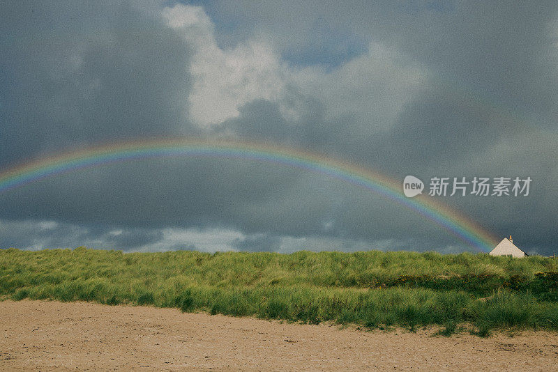 在遥远的苏格兰高地海滩上，高高的绿草和沙丘上的彩虹