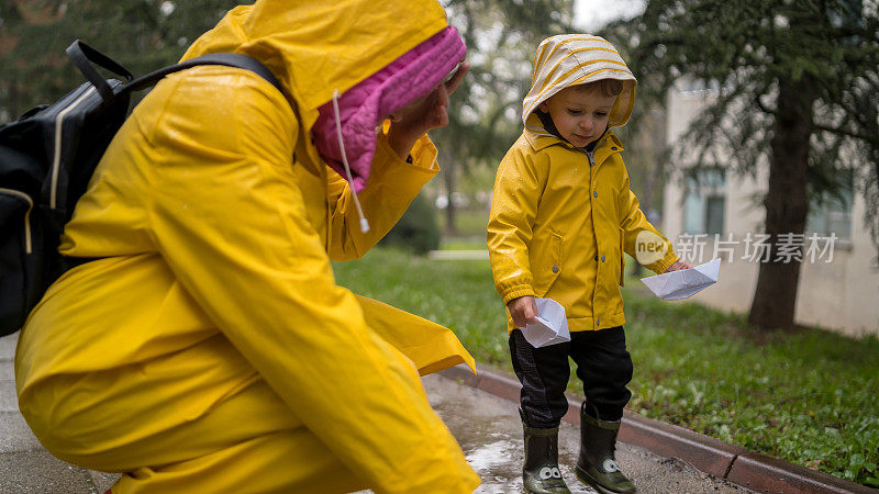 漂亮有趣的金发小孩带着橡皮鸭，在水坑里跳跃，在雨中玩耍