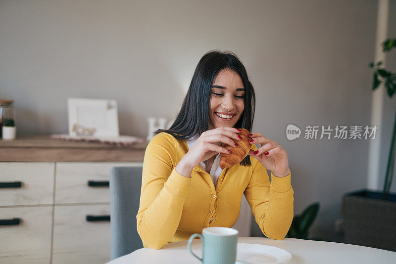 年轻女子在厨房吃牛角面包