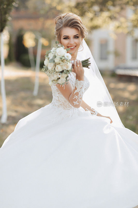 一位金发碧眼的新娘身穿白色长裙，手拿花束，面带微笑地走着