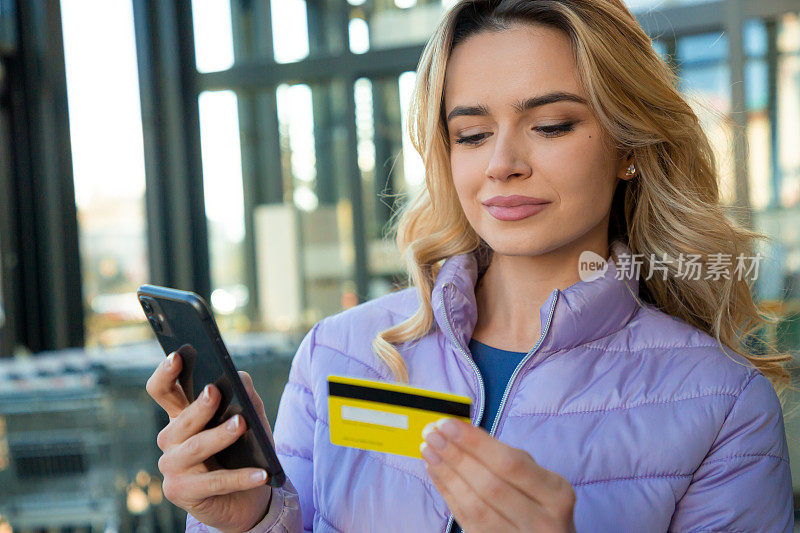 现代购物便利:金发女子用信用卡对着手机微笑