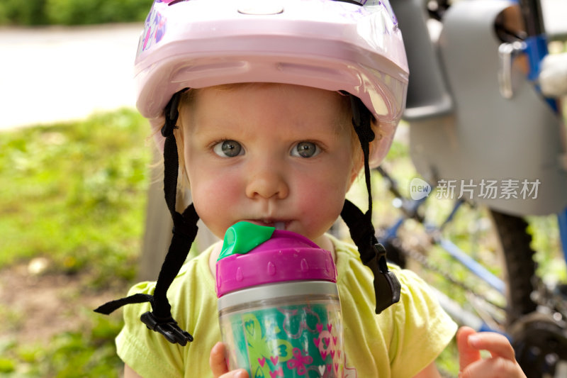 小女孩戴着自行车头盔喝水