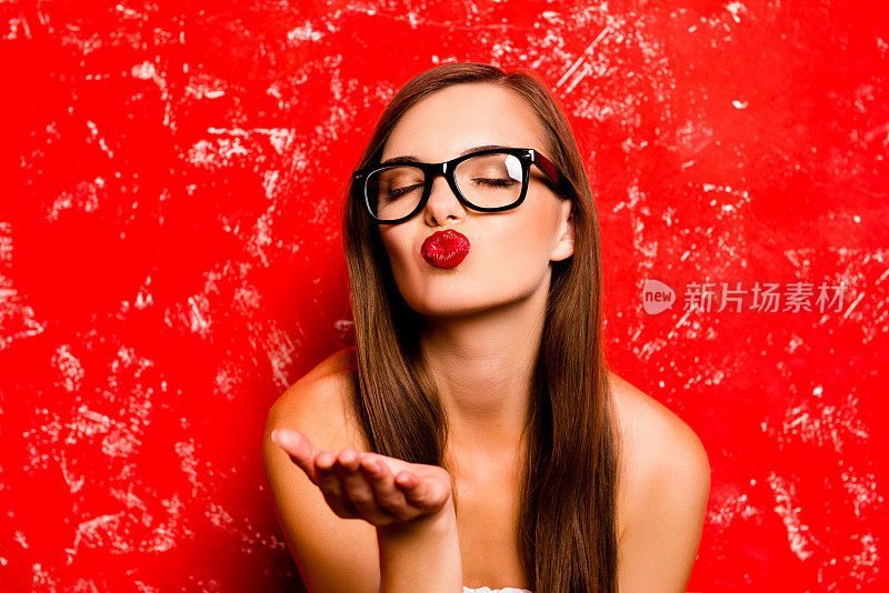 漂亮的女孩与眼镜送一个吻近红色的背景