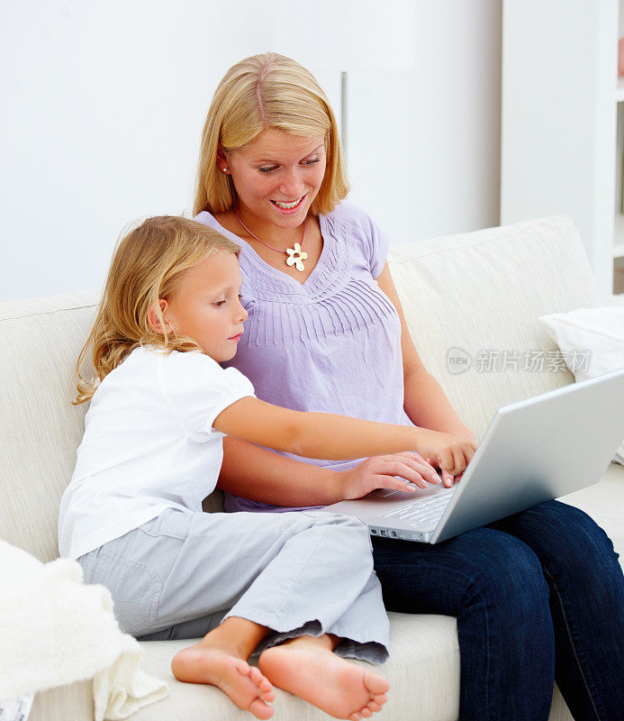 妈妈和她的女儿坐在沙发上使用笔记本电脑