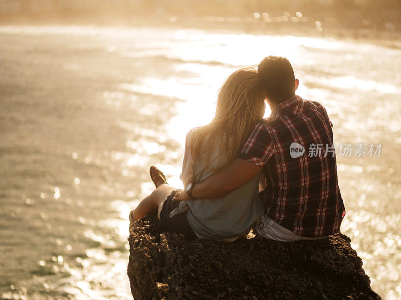一对夫妇从岩石上看日落的后视图。