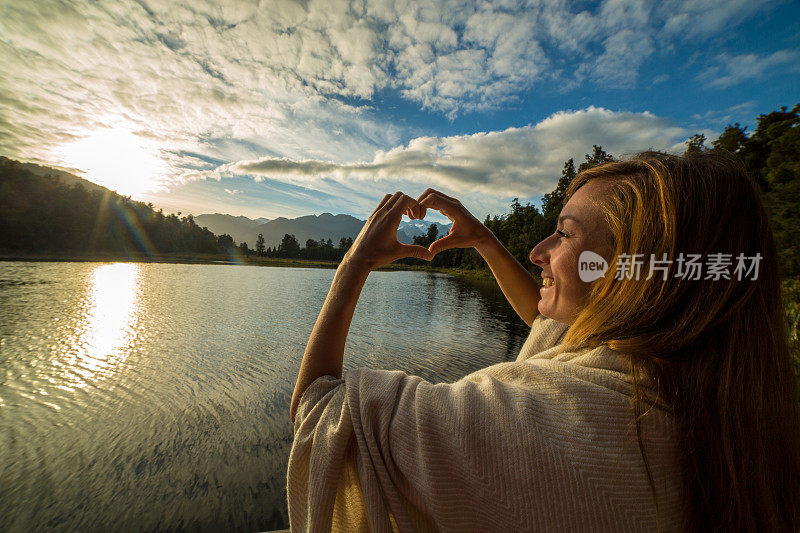 女性在山湖景观上做心形指架