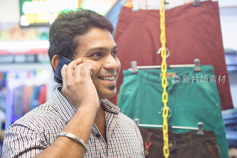 年轻的印度男子在购物中心用智能手机聊天
