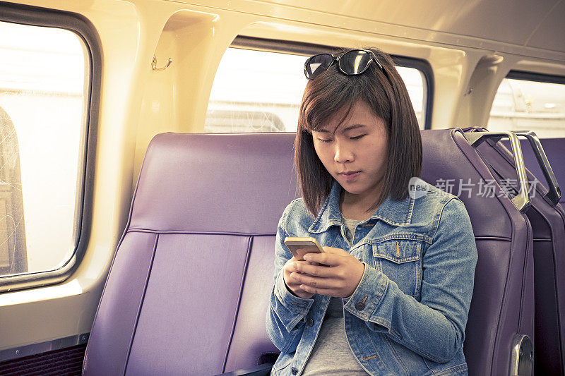 年轻的亚洲女学生在火车车厢里使用智能手机