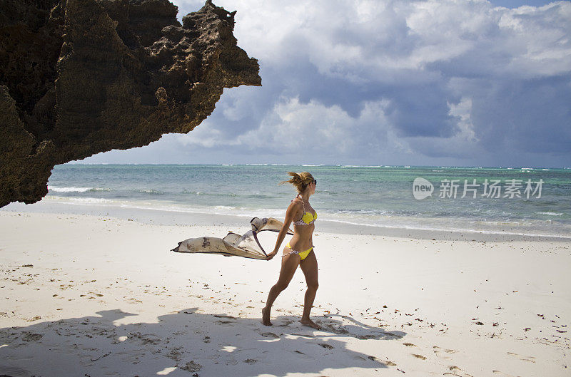 女人在比基尼与纱笼走在异国情调的海滩上