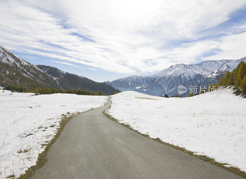 道路穿过雪山草地向下延伸