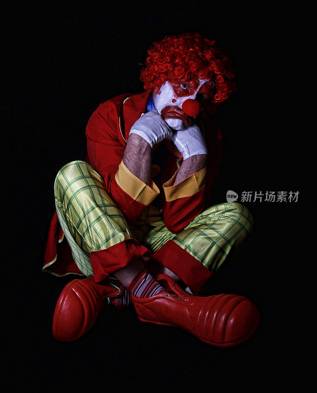 悲伤的小丑交叉双腿坐在地板上