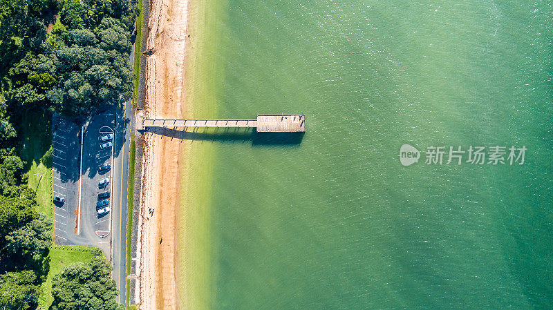 鸟瞰图在一个阳光明媚的海滩上有一个小码头和一个停车场沿路。奥克兰,新西兰