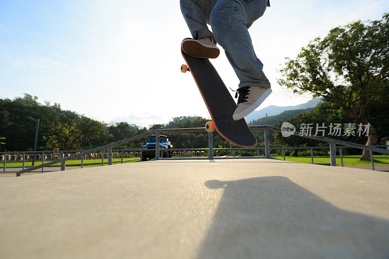 年轻的滑板运动员的腿练习奥利在滑板公园坡道