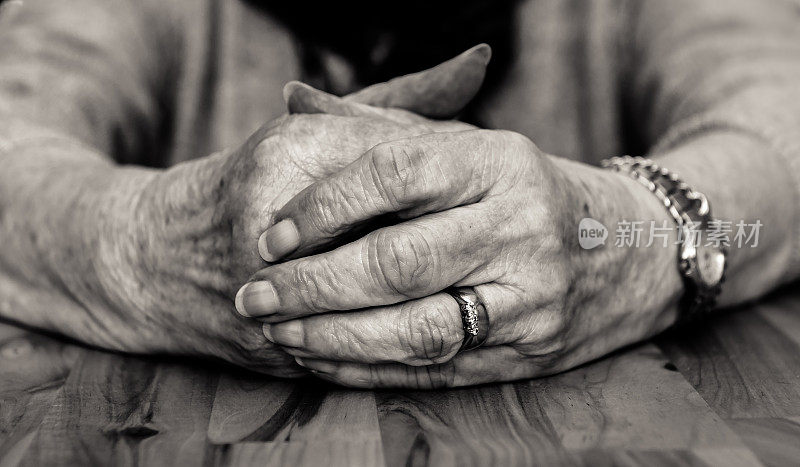 老妇人双手紧握的黑白图像。