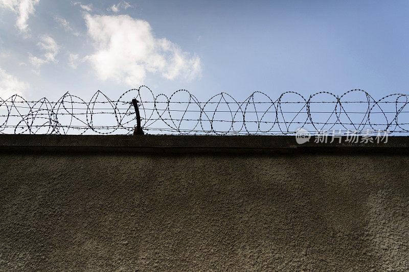 监狱的围墙是有刺的铁丝围栏，背景是蓝天