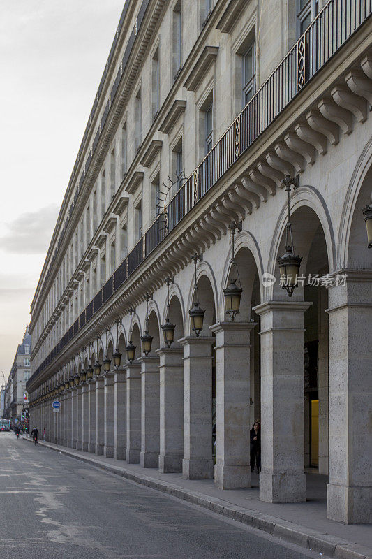在旧建筑的正面有一排带灯笼和柱子的拱门。透视图。法国巴黎的里沃利街