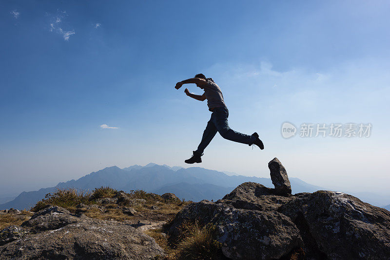 在山顶上举起手臂跳跃的男人