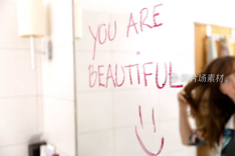女人用口红在镜子上写下“你很漂亮”来鼓励自己