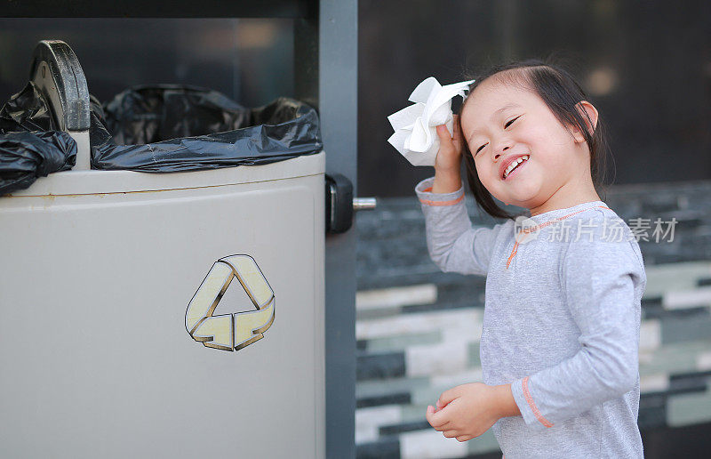 可爱的小女孩把垃圾放在户外的垃圾桶里。