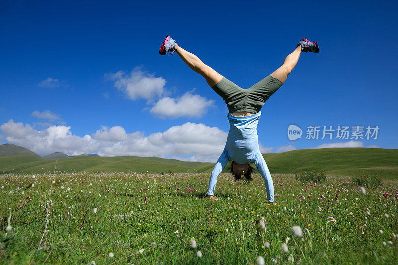一个女人在山顶的草地上做倒立