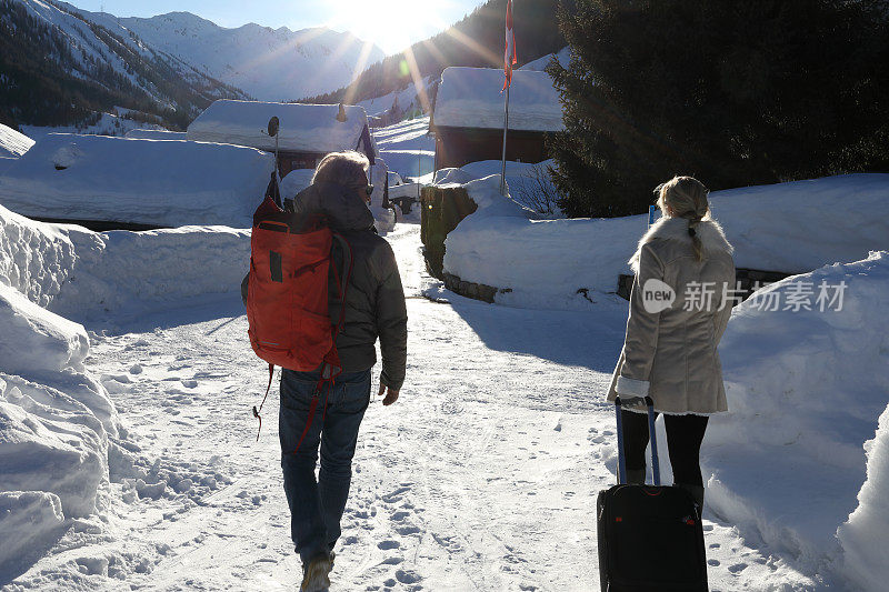 男人和女人拉着手提箱穿过白雪覆盖的村庄