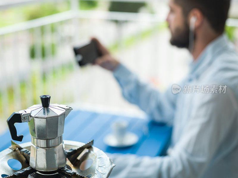 一个成年人在阳台上一边用手机一边喝浓缩咖啡