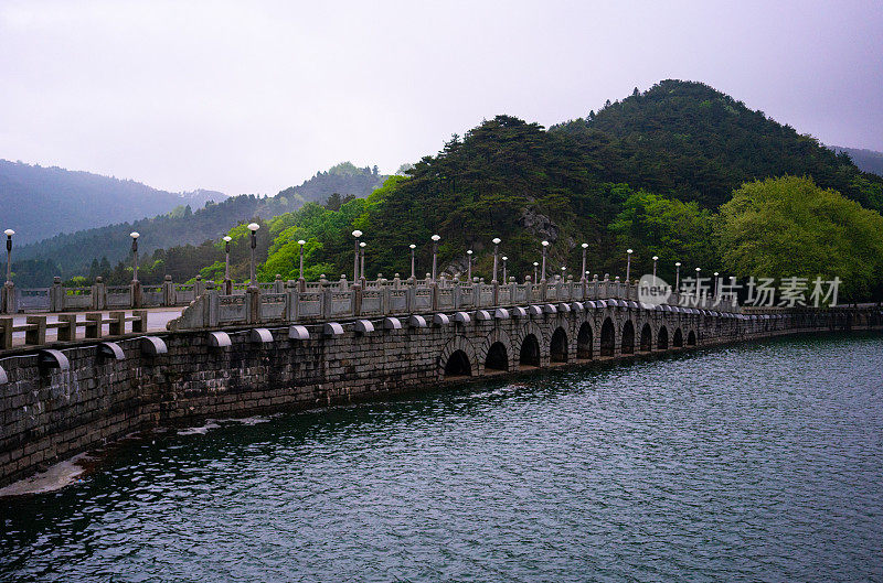 在中国江西庐山国家公园，一座带有绿林湖和青山的大坝上的中国桥