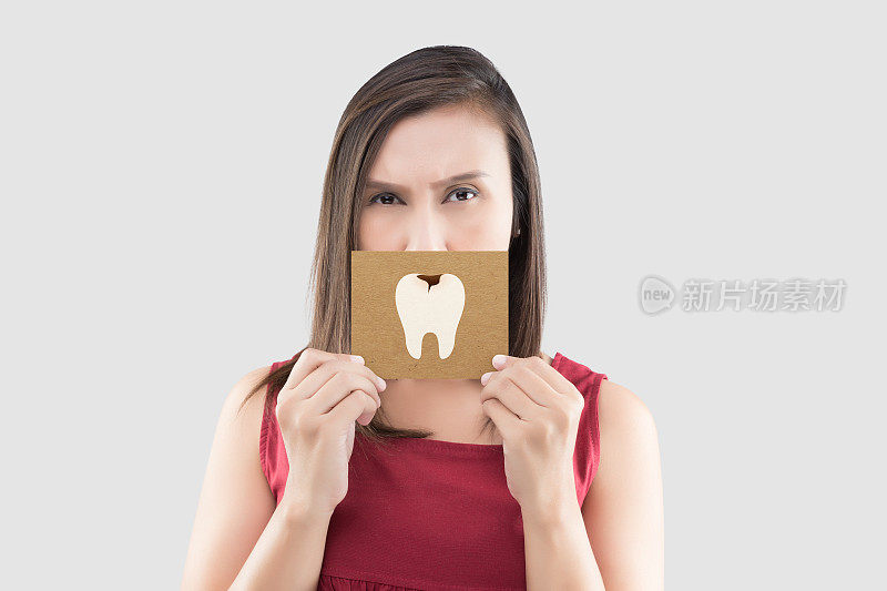 亚洲女子在红色衬衫拿着棕色纸与龋齿卡通图片他的嘴的灰色背景，有牙痛，与保健牙龈和牙齿的概念