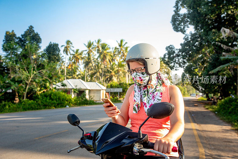 年轻女子在非洲骑摩托车旅行时查看手机