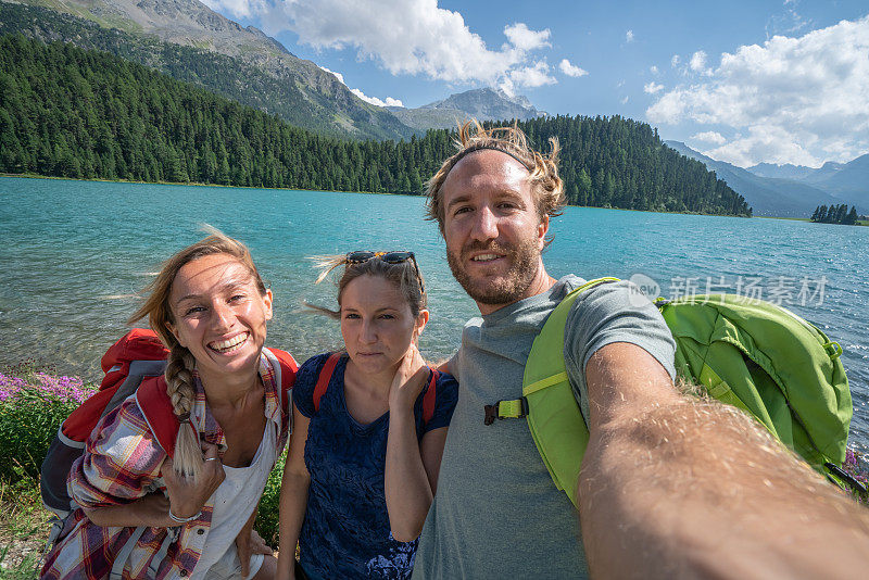 三个年轻人在夏天徒步旅行，在一个美丽的山湖边自拍