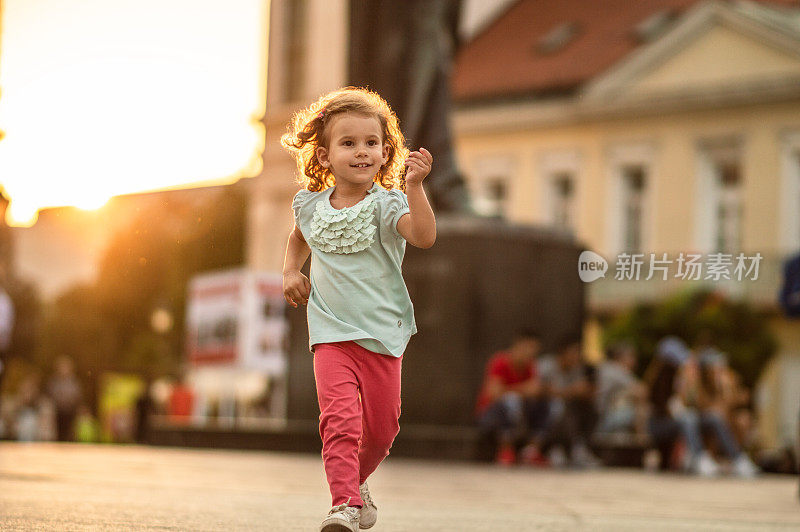 一个快乐的小女孩在金色的夕阳下奔跑在城市里